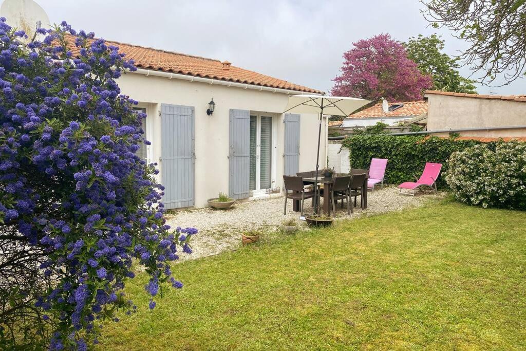 een tuin met een tafel en stoelen en paarse bloemen bij Charmante maison douillette de 65 m2 pour 4 pers. in Saint-Pierre-dʼOléron