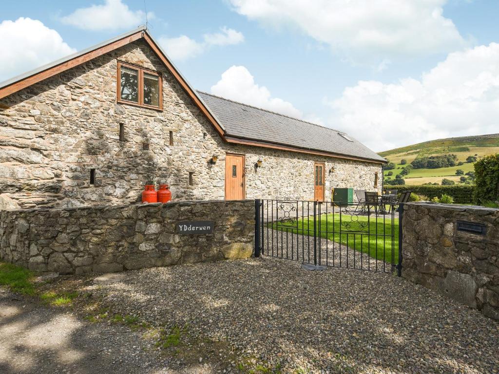a stone house with a stone fence in front of it at Y Dderwen in Pen-y-bont-fawr