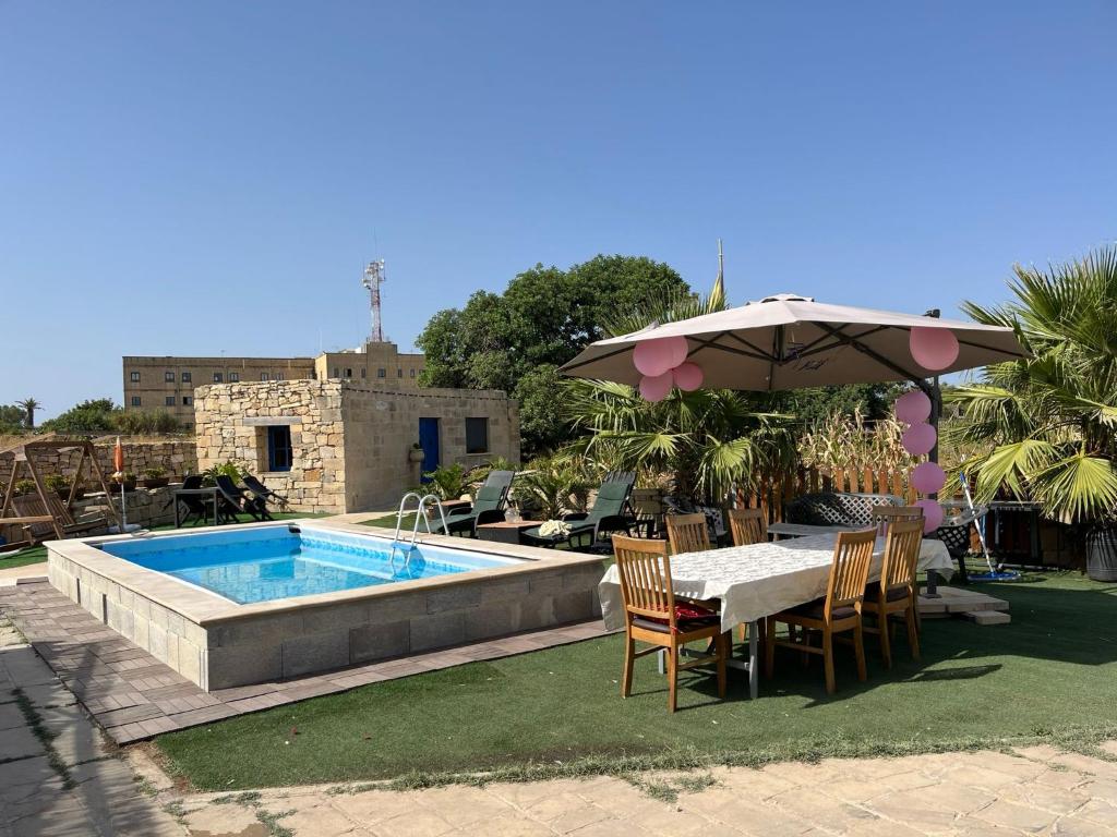 um pátio com uma mesa, um guarda-sol e uma piscina em The Cottage em Luqa