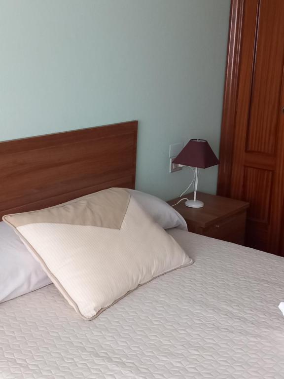 una cama con sábanas blancas y una lámpara sobre una mesa en PASEO DO MACEIRAS, en Redondela