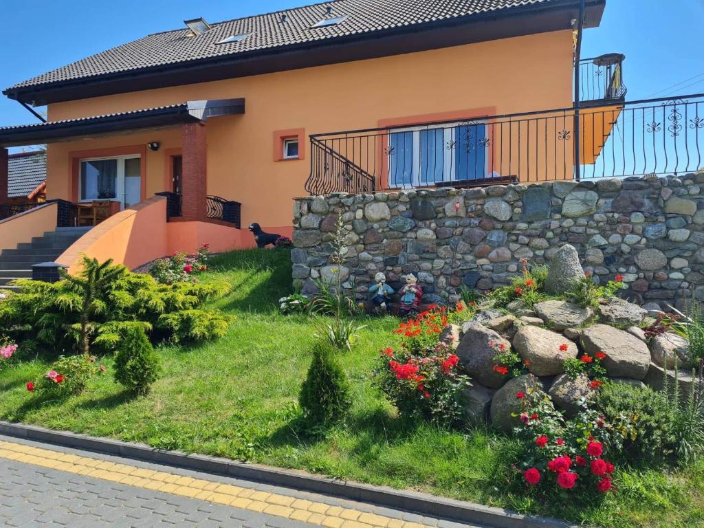 a house with a stone wall and flowers in the yard at Agroturystyka Barzowice in Darłowo