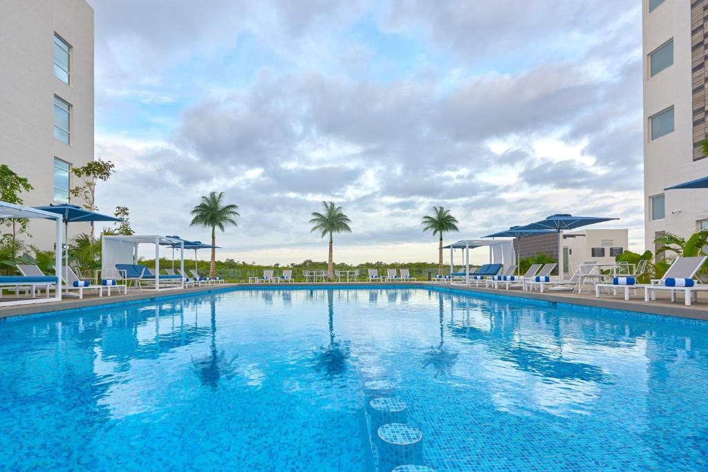 una gran piscina con sillas azules y palmeras en City Express Plus by Marriott Cancun Aeropuerto Riviera en Cancún