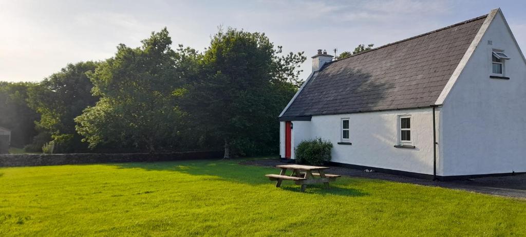 una pequeña casa blanca con una mesa de picnic en el patio en Louisburgh Cottages, en Louisburgh