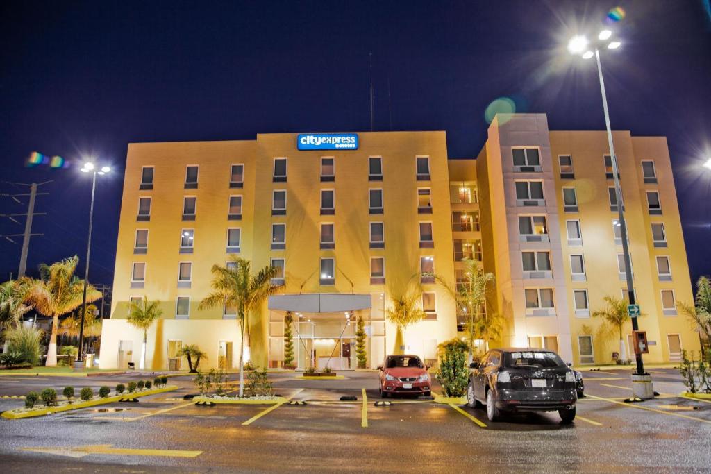 un hotel con coches estacionados en un estacionamiento por la noche en City Express by Marriott Celaya Parque, en Celaya