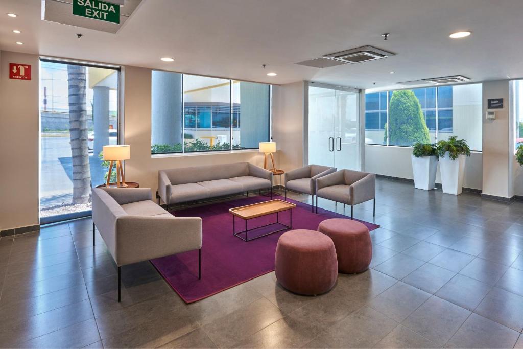 un vestíbulo de oficina con sofás, mesas y ventanas en City Express by Marriott San Luis Potosi Zona Universitaria, en San Luis Potosí
