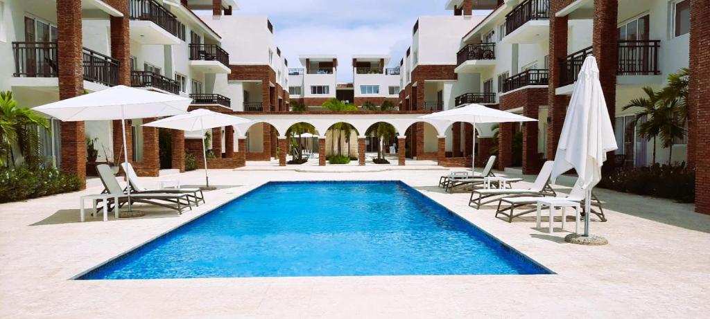 a swimming pool with chairs and umbrellas next to a building at Deluxe Condo/1BR-1BT/Close to Beach/Pool View in Punta Cana