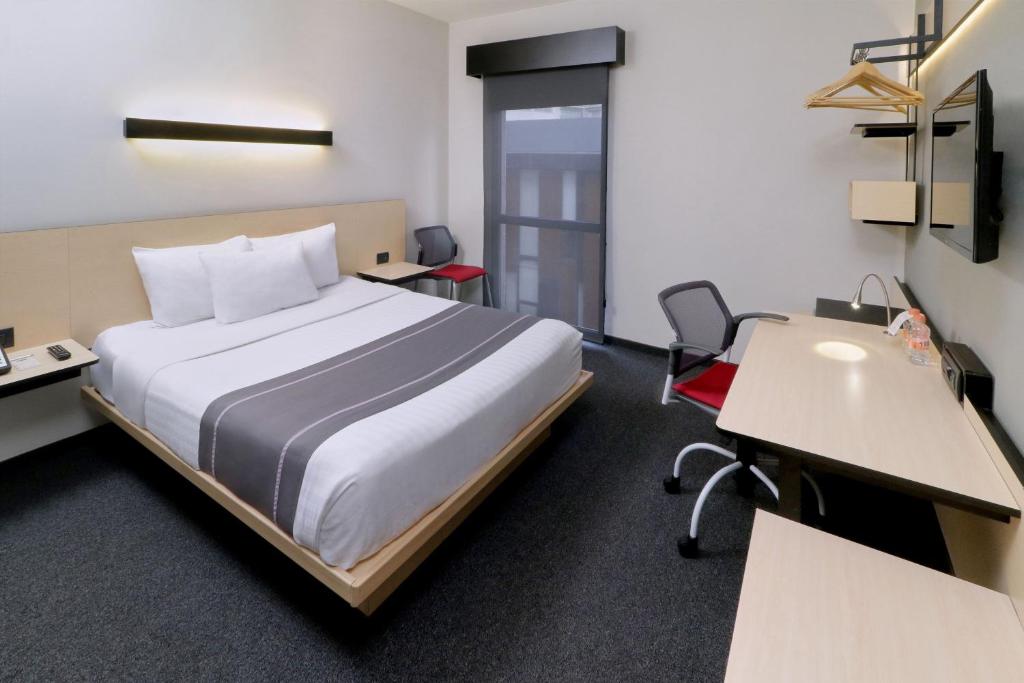 a hotel room with a bed and a desk and chairs at City Express Plus by Marriott Monterrey Nuevo Sur in Monterrey