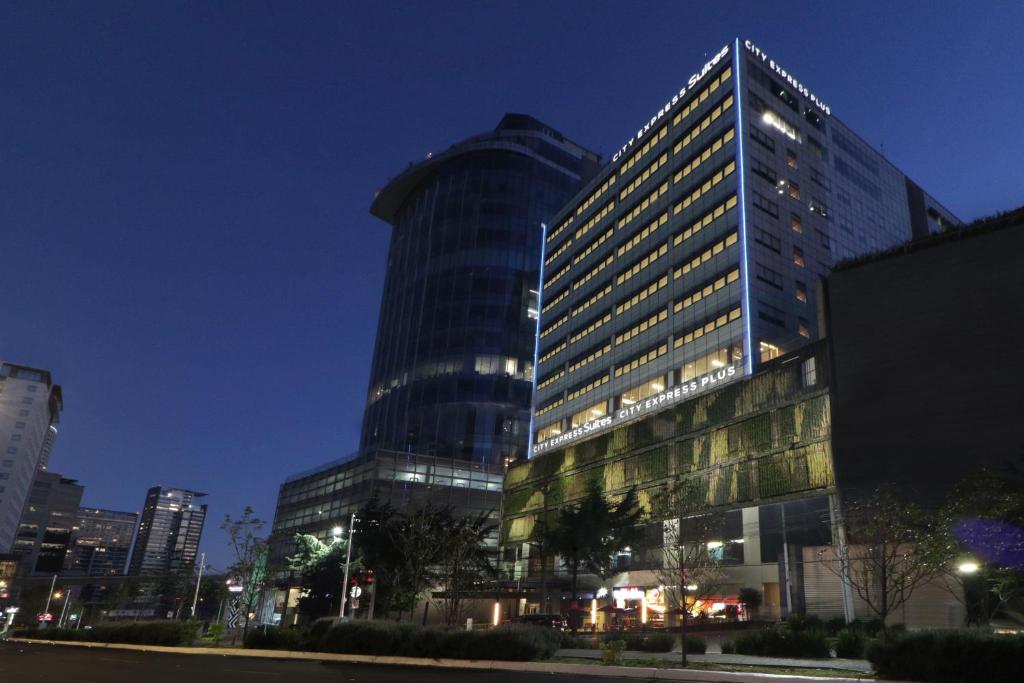 um edifício alto com luzes acesas numa cidade à noite em City Express Suites by Marriott Santa Fe em Cidade do México