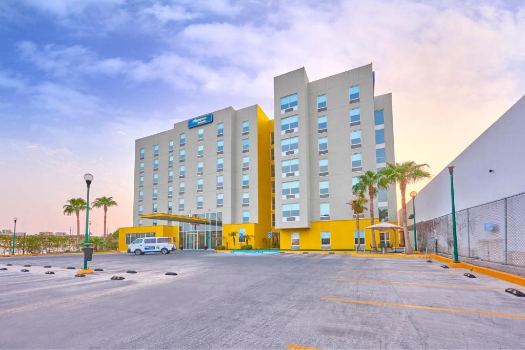 un parking de l'hôtel avec un bâtiment jaune et blanc dans l'établissement City Express by Marriott Mexicali, à Mexicali