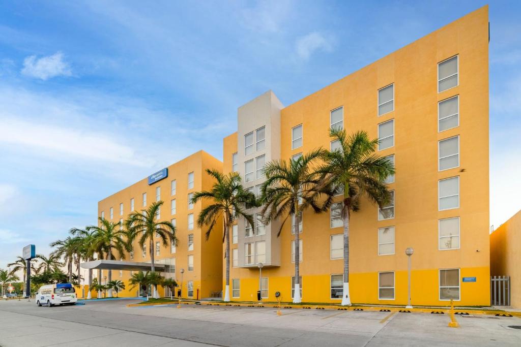 un bâtiment jaune avec des palmiers devant lui dans l'établissement City Express by Marriott Ciudad del Carmen, à Ciudad del Carmen