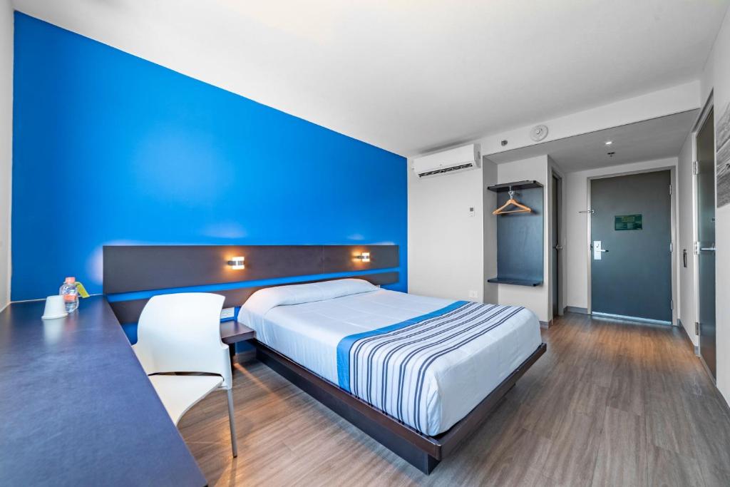 1 dormitorio con cama y pared azul en City Express Junior by Marriott Merida Altabrisa, en Mérida