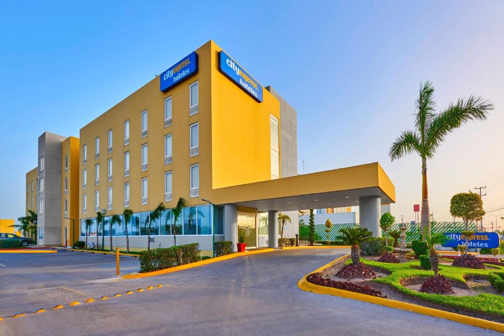 un grand bâtiment jaune avec des palmiers devant lui dans l'établissement City Express by Marriott Reynosa, à Reynosa