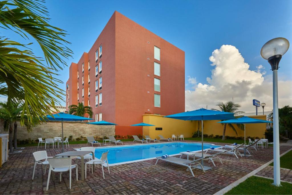un hotel con piscina, sillas y sombrillas en City Express Junior by Marriott Cancun, en Cancún