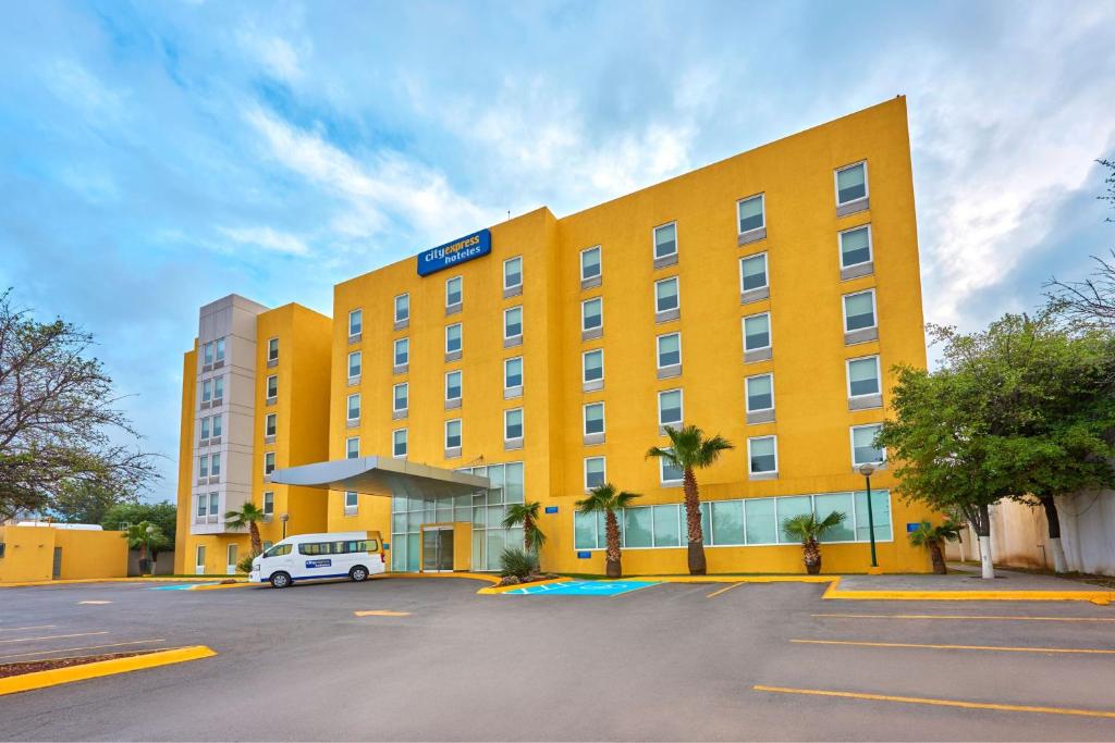 un hôtel jaune avec une camionnette blanche garée dans un parking dans l'établissement City Express by Marriott Saltillo Sur, à Saltillo