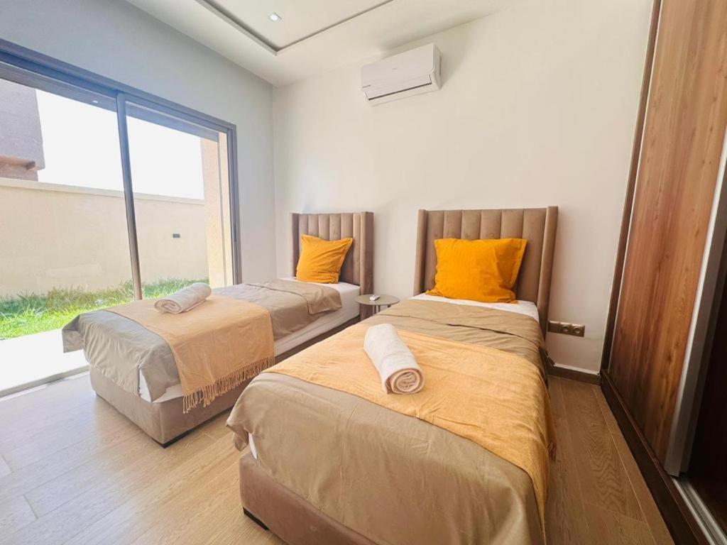 2 Betten mit orangefarbenen Kissen in einem Zimmer mit Fenster in der Unterkunft Villa dream oujda in Oujda