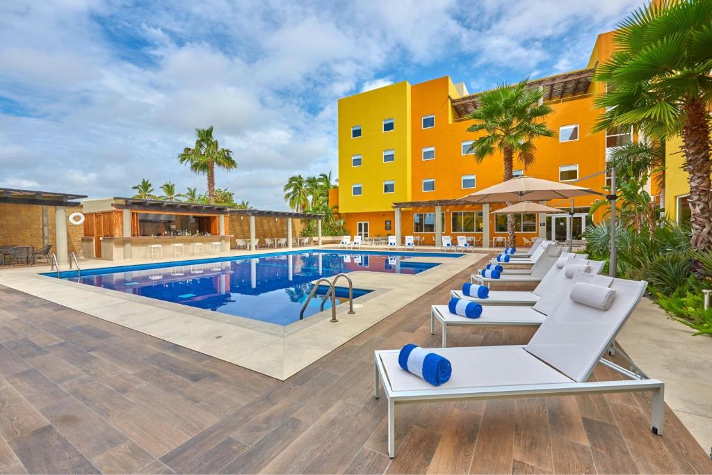 a resort pool with lounge chairs and a hotel at City Express Plus by Marriott Cabo San Lucas in Cabo San Lucas