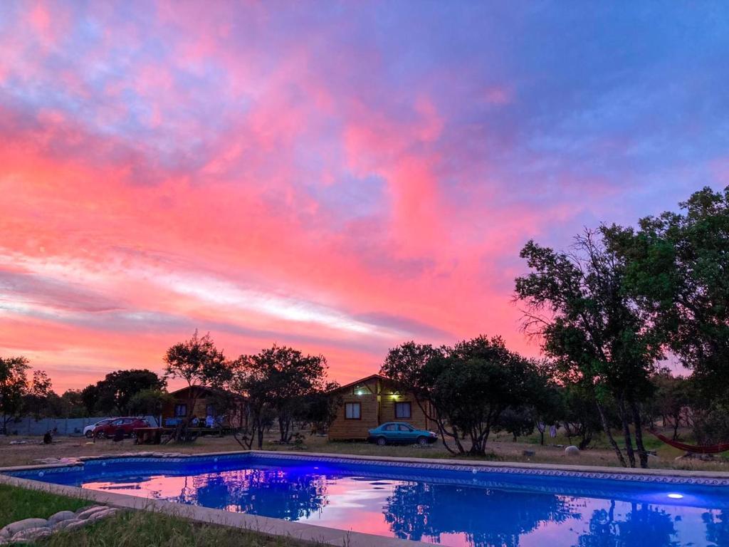 una puesta de sol sobre una piscina frente a una casa en Cabañas Llepu, en Linares