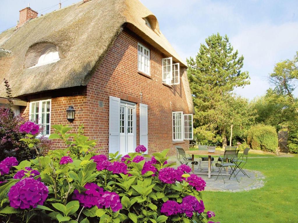 a brick house with a thatched roof with purple flowers at Zollhaus in Kampen