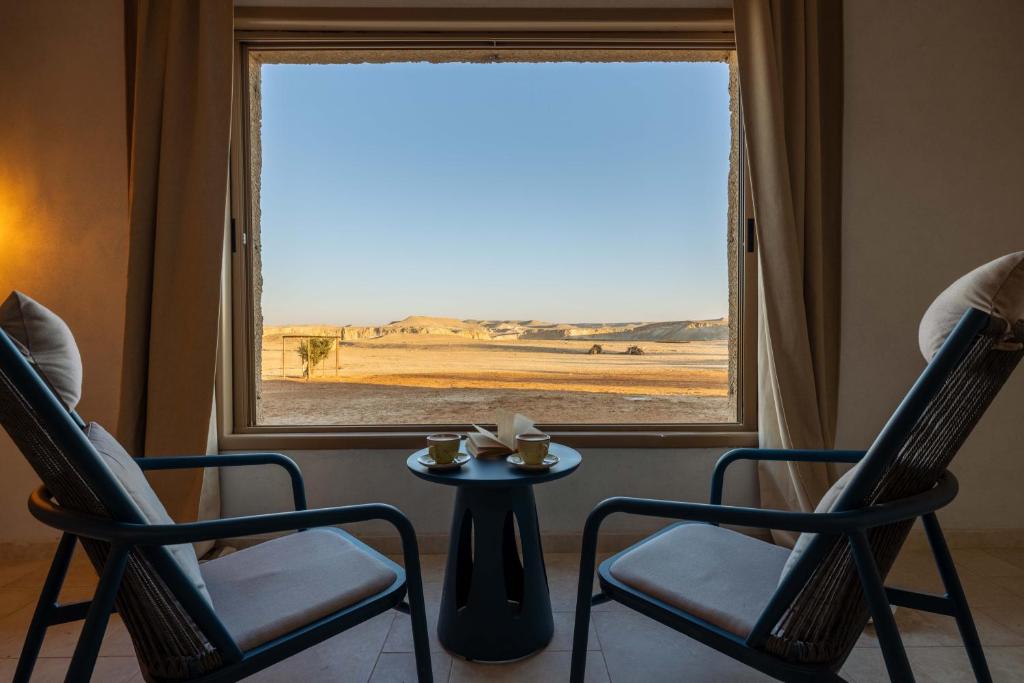 two chairs and a table in front of a window at Shermans Hotel in Sde Boker