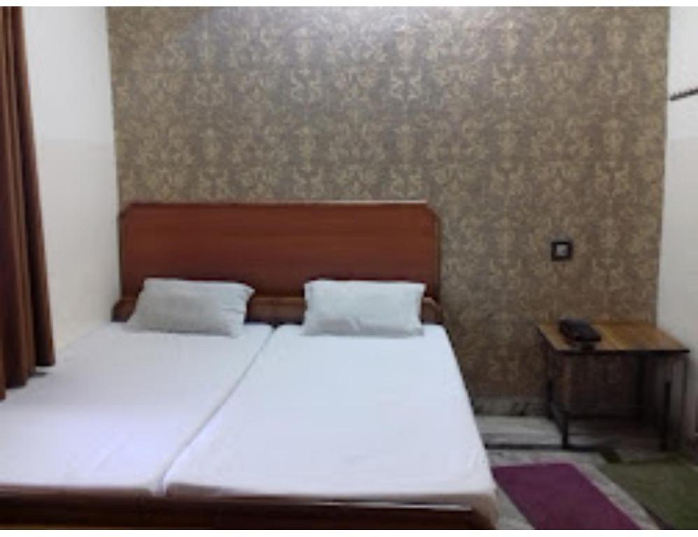 a bedroom with a white bed with a wooden headboard at Hotel Shree Ganesh, Jhansi in Jhānsi