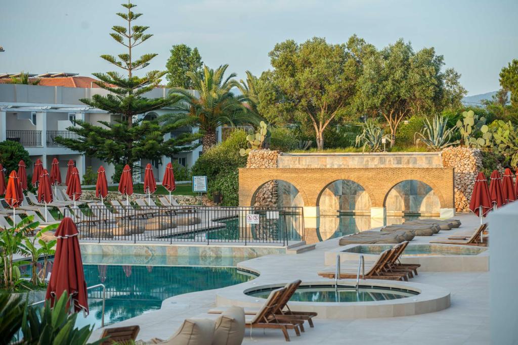 una piscina con sillas y sombrillas rojas en Bitzaro Grande Hotel & Suites, en Kalamaki