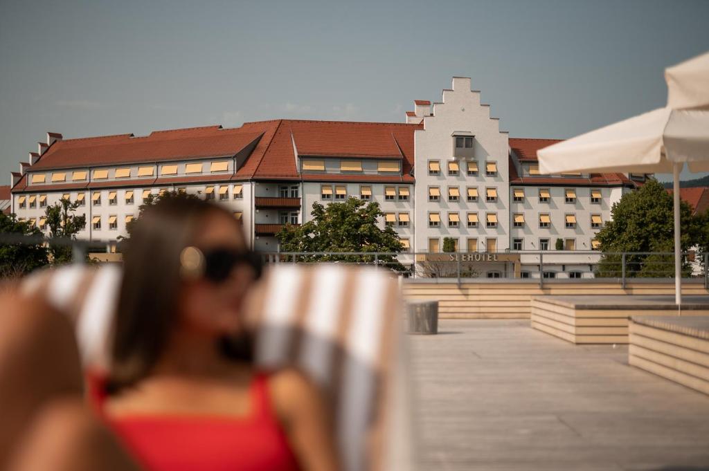 eine Frau, die auf einem Stuhl vor einem Gebäude sitzt in der Unterkunft Seehotel am Kaiserstrand in Lochau