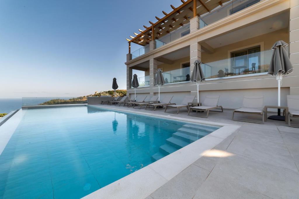 uma piscina do hotel com cadeiras e vista para o oceano em Sky View Suites Kefalonia em Vóvikes