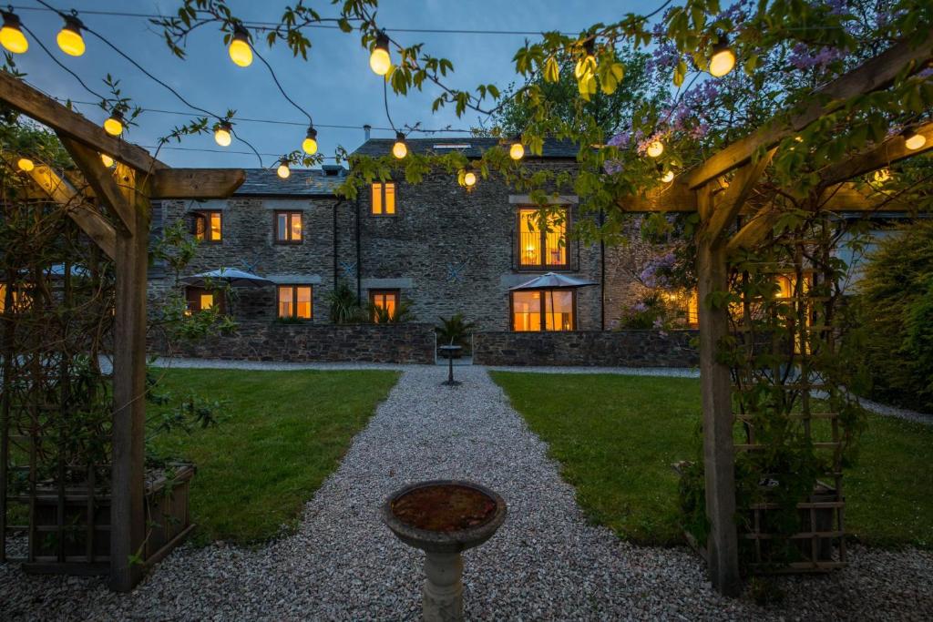 a garden with a stone house with a pergola at Threshing Barn at East Trenean Farm -Stunning Cornish Cottage sleeping 6 with hot tub, private garden, rural views and EV facilities in East Looe