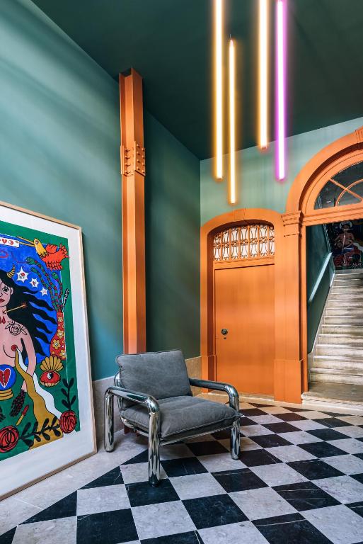 A colourful lobby or landing combines a checkered floor, artwork, armchair and staircase.