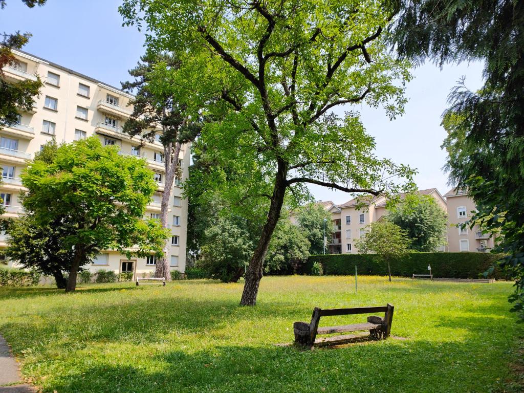 un banco del parque sentado en el césped cerca de un árbol en L'Edelweiss Campus & Parking privé securisé, en Gières