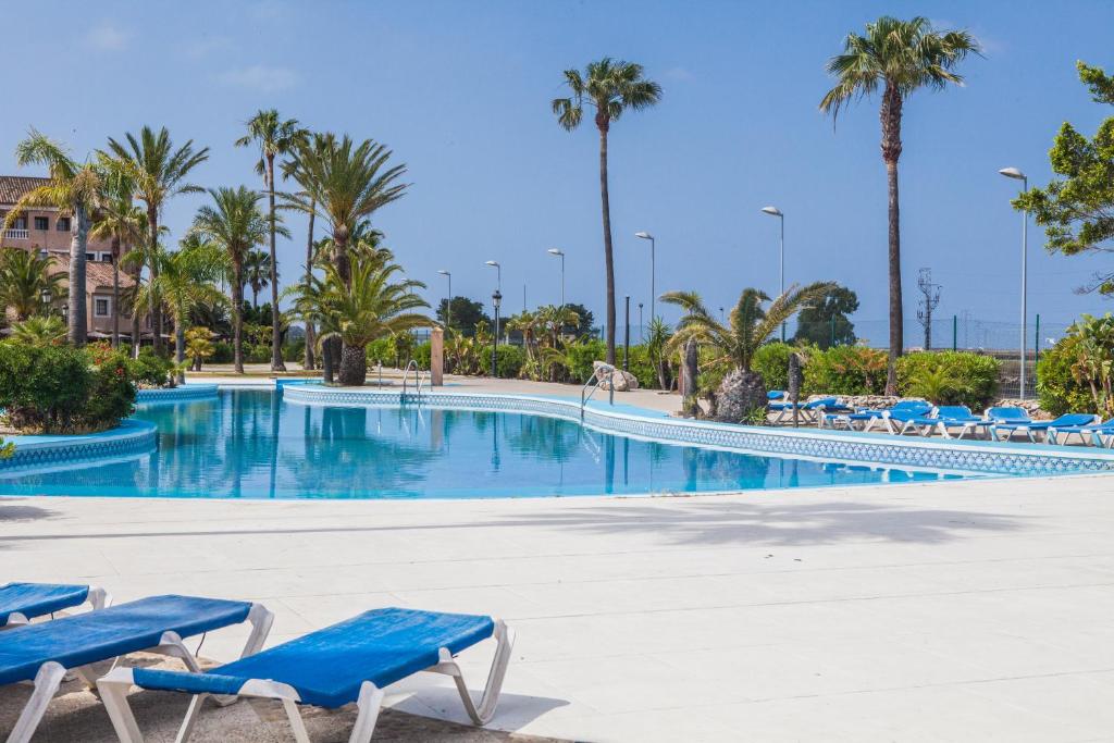 una piscina con sillas azules y palmeras en Estudios Turísticos Bahia Sur, en San Fernando