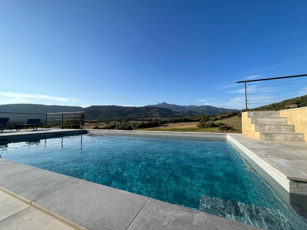 a swimming pool with blue water and mountains in the background at Hôtel Guest House Baritedda in Pianottoli-Caldarello