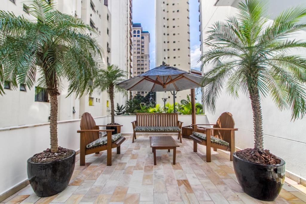a patio with palm trees and benches and an umbrella at Tabas - Victoria Place - Itaim Bibi in Sao Paulo