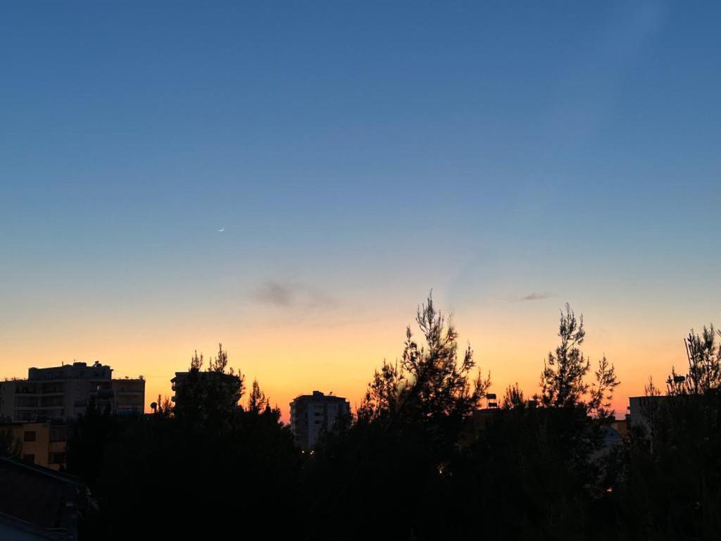 een zonsondergang boven een stad met bomen op de voorgrond bij Vlora Central & Comfy Apartment in Vlorë