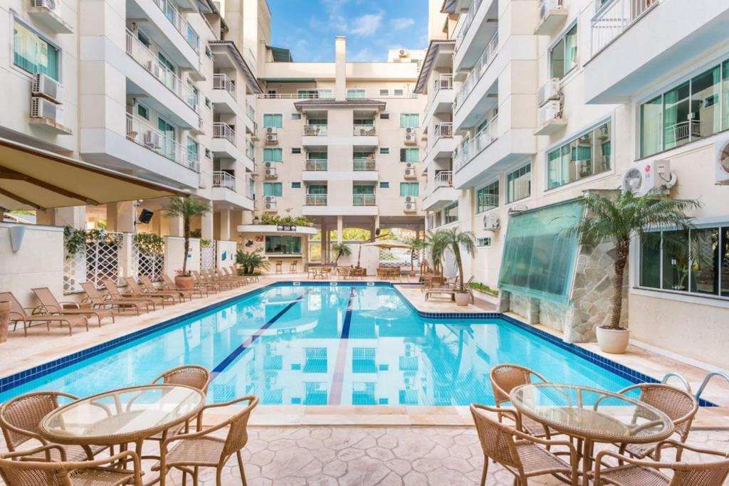 een zwembad met tafels en stoelen naast een gebouw bij Flat com Piscina Térmica no Bombinhas Summer Beach in Bombinhas