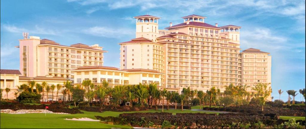 a large building with palm trees in front of it at Mission Hills Resort Haikou in Haikou