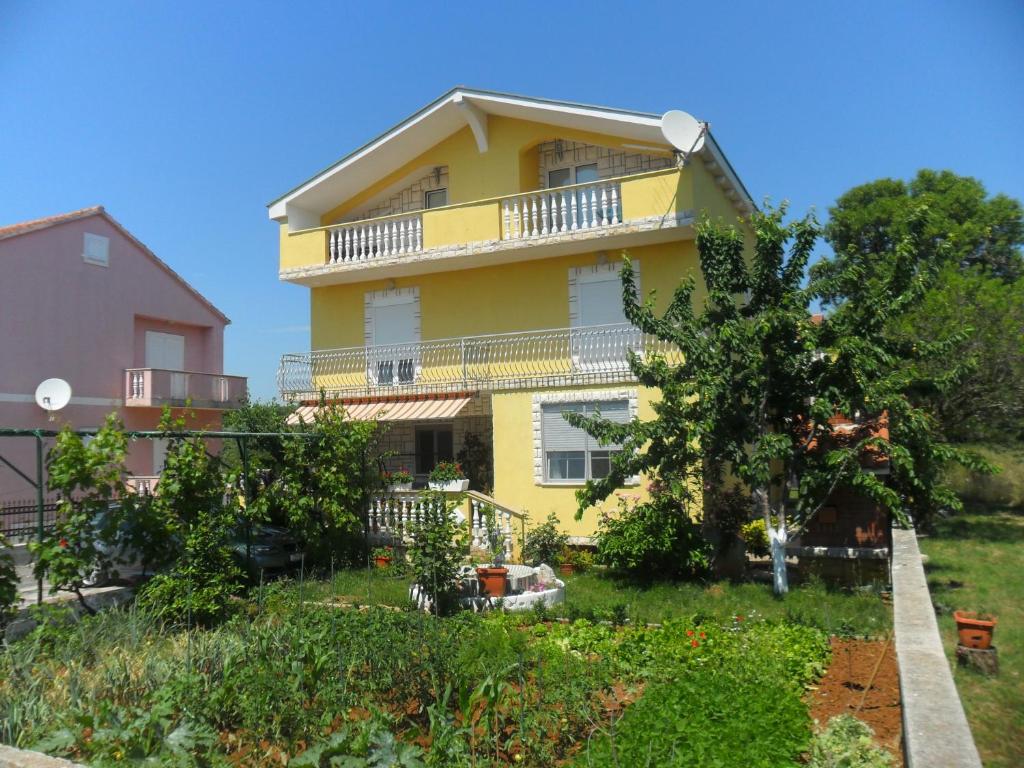 ein gelbes Haus mit einem Balkon und Bäumen in der Unterkunft Apartments Marina in Sukošan