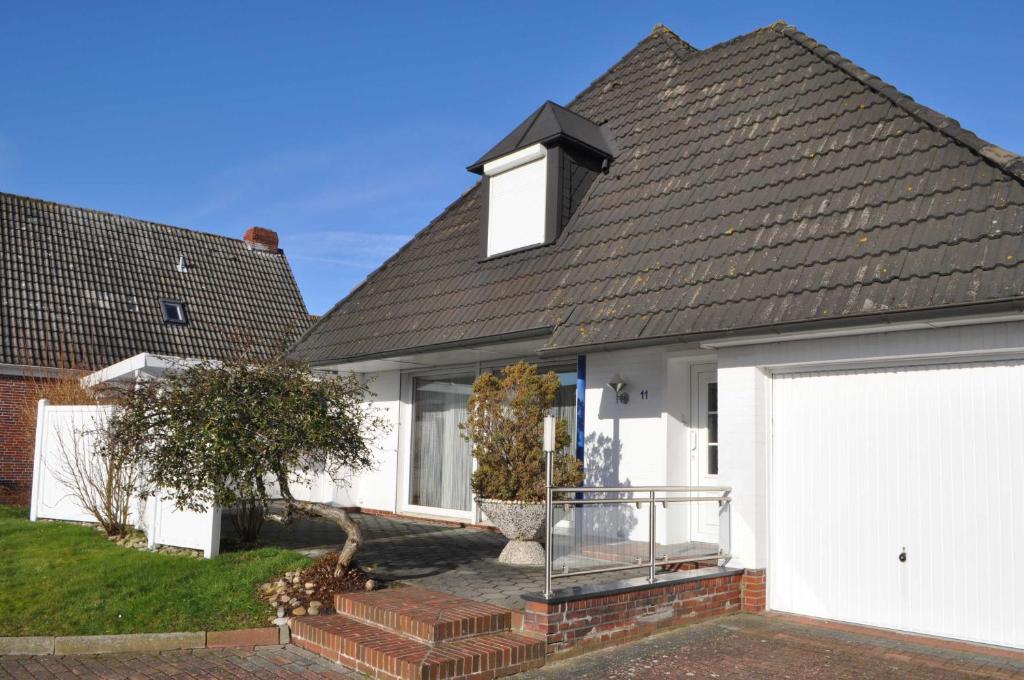 uma casa branca com um telhado preto e uma garagem branca em Nr 44 - Ferienwohnung Caspersweg em Carolinensiel