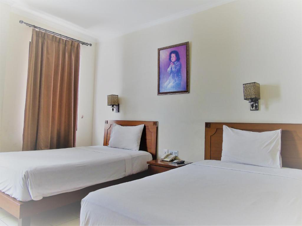 2 camas en una habitación de hotel con sábanas blancas en Pia Hotel, en Cirebon