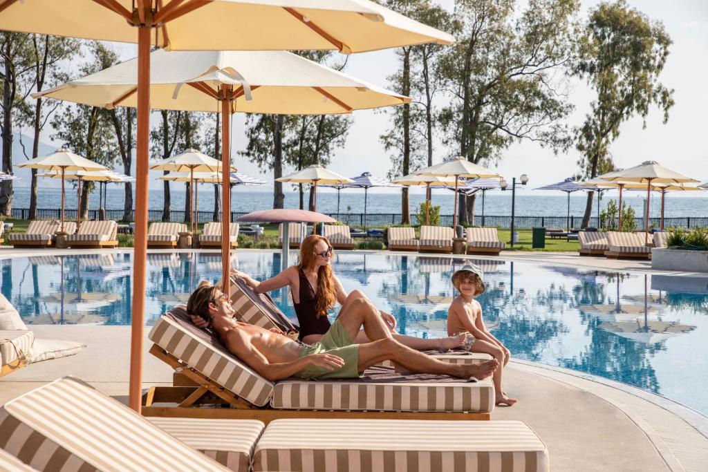 a family sitting on lounge chairs by the pool at a resort at Kerkyra Blue Hotel & Spa by Louis Hotels in Corfu