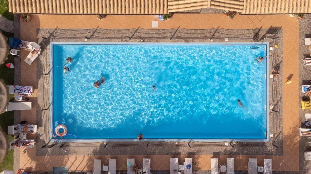 an overhead view of people swimming in a large swimming pool at iH Hotels Le Zagare Resort in Villasimius