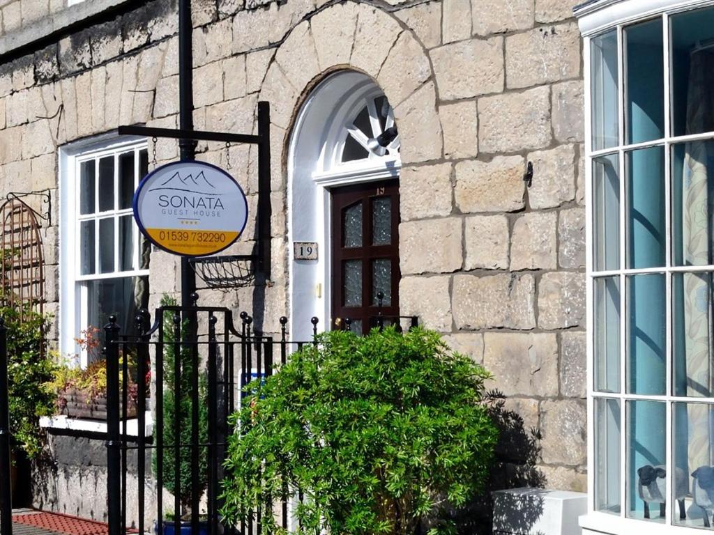 a sign in front of a building with a door at Sonata Guest House in Kendal