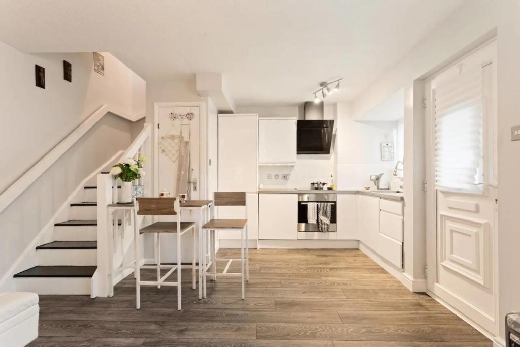 a white kitchen with stairs and a table and chairs at Snug & Cosy Home In Thamesmead Overlooking A Park in Thamesmead
