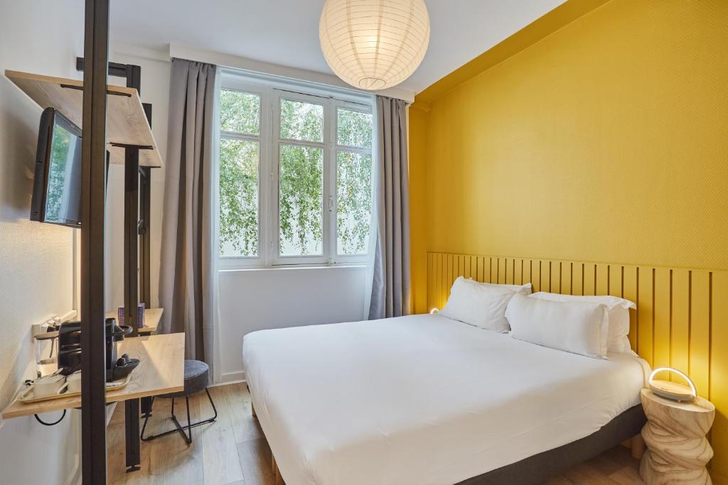 sypialnia z białym łóżkiem i żółtą ścianą w obiekcie Hôtel Beauquartier Montmartre w Paryżu