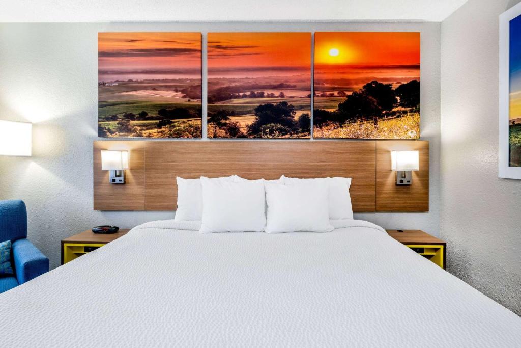 a bed in a hotel room with four paintings on the wall at Days Inn by Wyndham Sioux Falls Airport in Sioux Falls