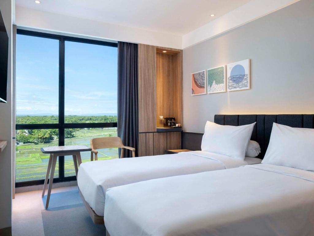 a hotel room with two beds and a table and a window at ibis Yogyakarta International Airport Kulon Progo in Yogyakarta