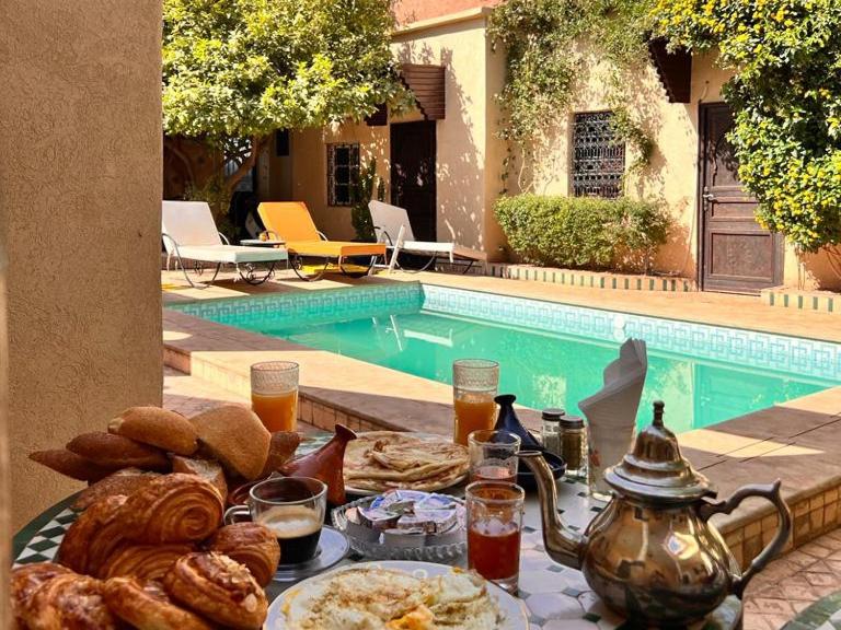 einen Tisch mit einem Tablett mit Frühstücksspeisen neben einem Pool in der Unterkunft Riad Rime Garden Marrakech in Marrakesch