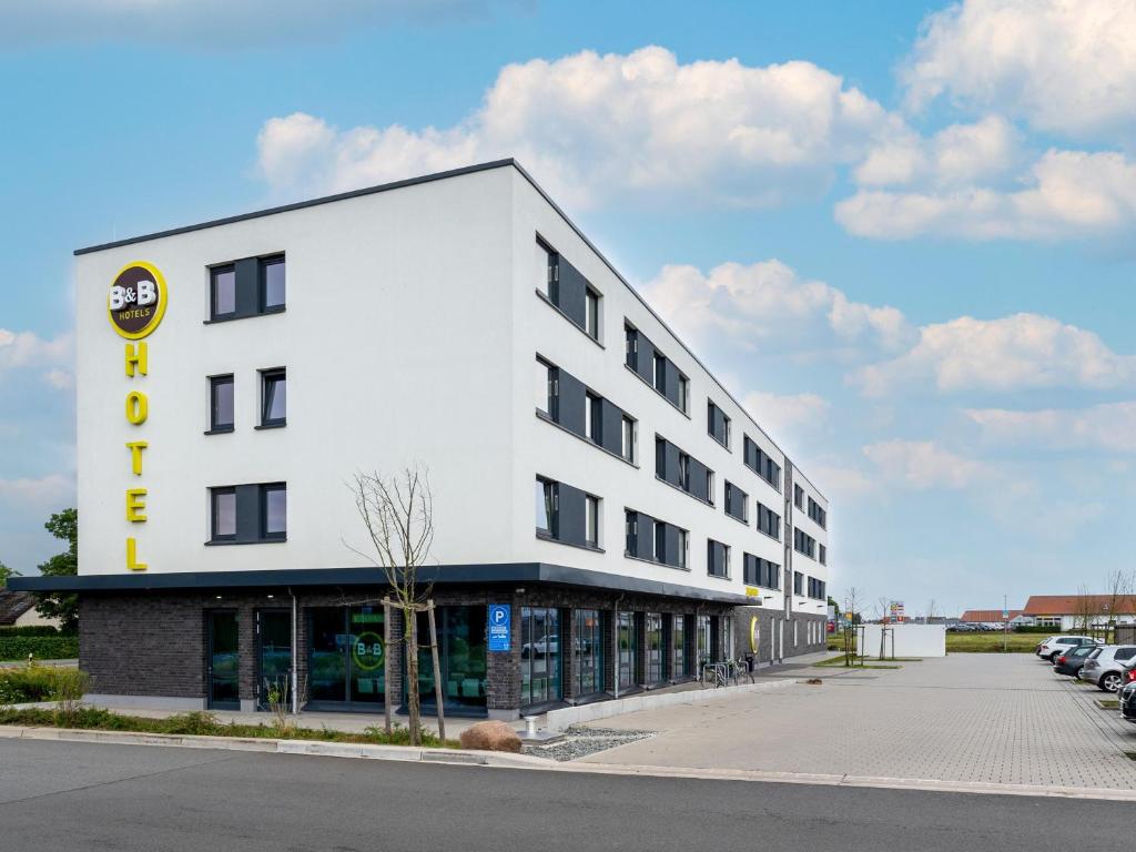 a large white building with a parking lot at B&B Hotel Wolfsburg-Weyhausen in Wolfsburg