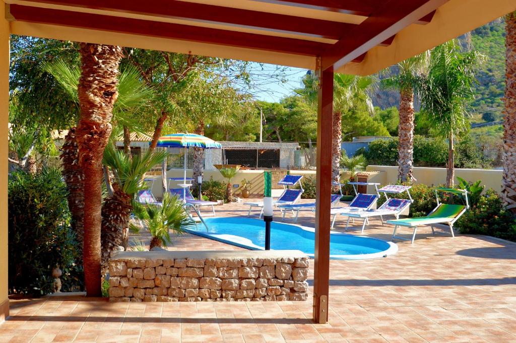 a patio with a swimming pool with chairs and an umbrella at Villa Minoa con piscina in San Vito lo Capo