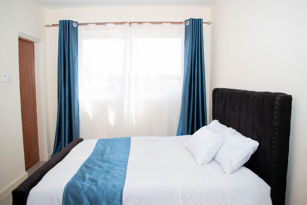 1 dormitorio con 1 cama con cortinas azules y ventana en Staycation with les, en Eldoret